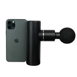 A compact and portable black massage device next to a smartphone, indicating its size and scale.